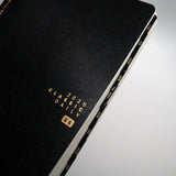 Aura Estelle Skinny Tab Stickers Black Gold Black Gold skinny tabs applied to black notebook edge
