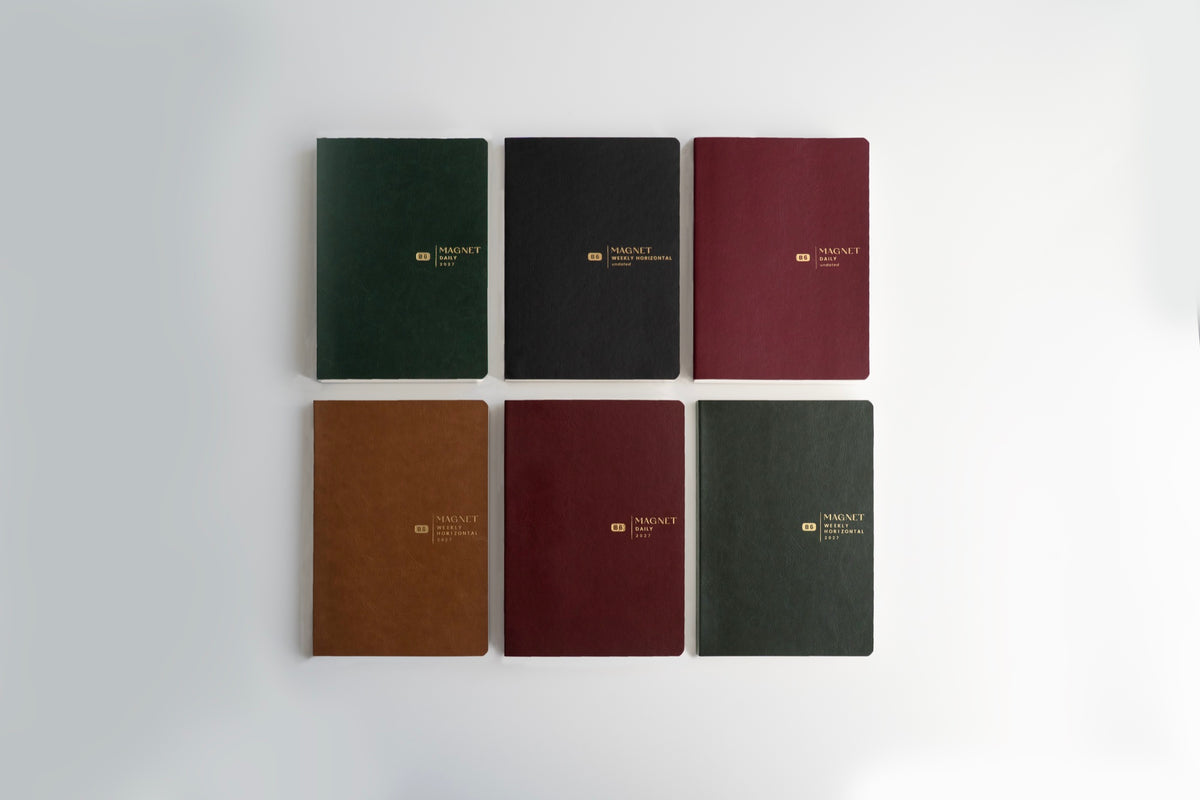 Six Aura Estelle 2027 magnet planners laid out in dark green, black, red and brown