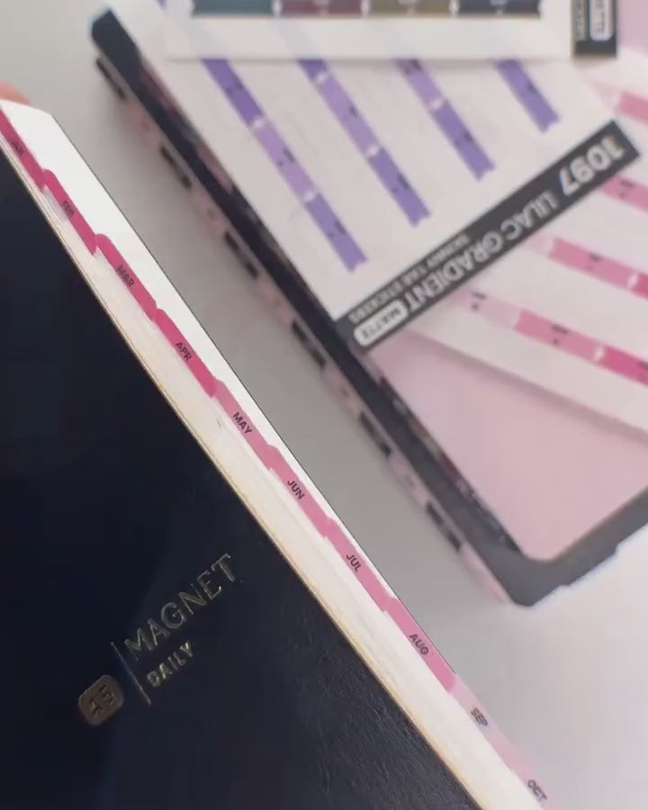 A planner with pink skinny tabs down the page edge, beside sheets of tab stickers